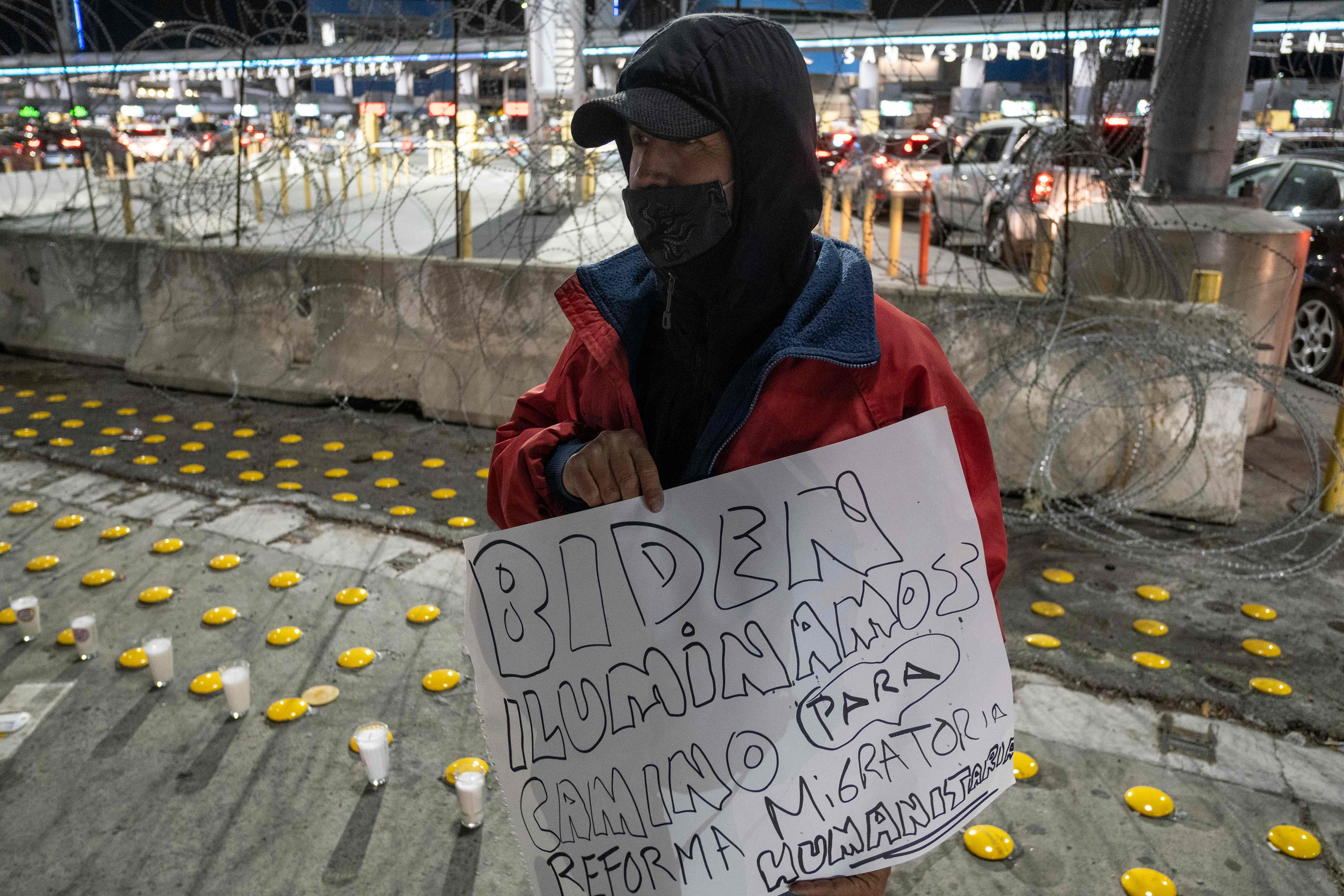 Un migrante sostiene un cartel que dice "Biden: ilumine el camino para una reforma migratoria humana", como se manifiestan defensores y migrantes en el puerto de cruce de San Ysidro durante una vigilia llamada "Camino hacia una reforma migratoria humana", en Tijuana, estado de Baja California, México el 19 de enero de 2021, 