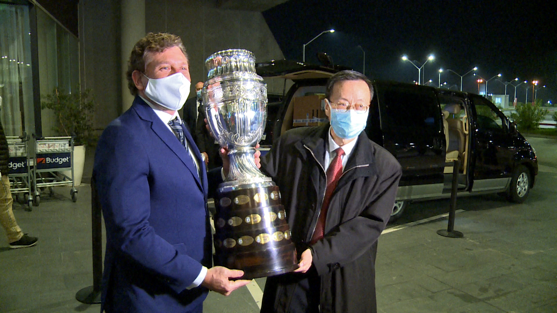 Screen grab showing Conmebol president, Paraguayan Alejandro Dominguez (L), and Chinese Ambassador in Uruguay Wang Gang, holding the Copa America trophy upon the arrival of 50,000 doses of the Chinese Sinovac vaccine against COVID-19 at the Carrasco International Airport in Ciudad de la Costa, Uruguay, on April 28, 2021. - The vaccines were donated by Chinese laboratory Sinovac to immunize South American football players, who will take part in the Conmebol Copa America and other tournaments. (Photo by Nicolas GARCIA / AFPTV / AFP) (Photo by NICOLAS GARCIA/AFPTV/AFP via Getty Images)