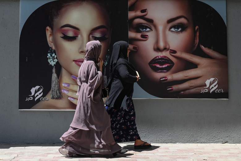 Mujeres vestidas con burka pasan junto a una valla publicitaria colocada en la pared de un salón de belleza en Kabul el 7 de agosto de 2021.